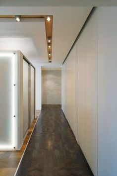 an empty hallway with white walls and wood flooring is lit by recessed lights