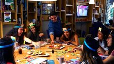 a group of people sitting around a wooden table with plates of food on top of it