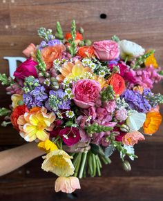 a bouquet of colorful flowers is held by a woman's hand in front of a wooden wall