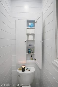 a white toilet sitting inside of a bathroom next to a shelf filled with towels and other items