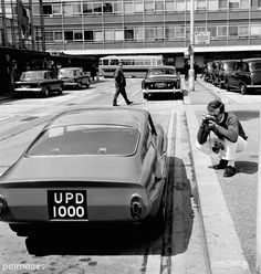 black and white photograph of people walking down the street with cars parked in front of them