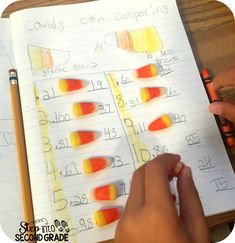 a child's hand is writing on paper with candy corn colors in front of them