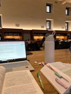 an open book sitting on top of a wooden table next to a laptop and pen