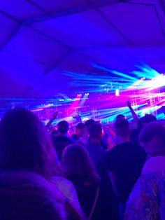 a group of people standing under a tent at a music festival with bright lights on the ceiling