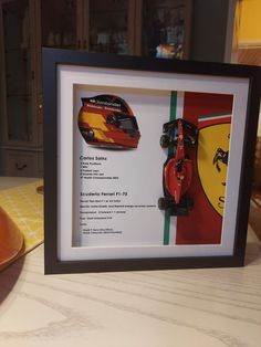 a framed photograph of a race car and helmet on the table next to a plate