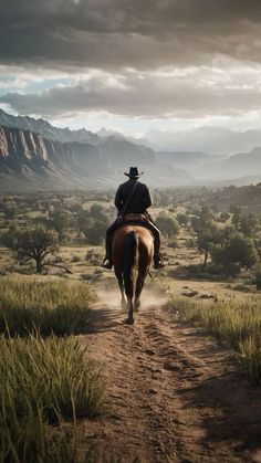 a man riding on the back of a brown horse down a dirt road under a cloudy sky