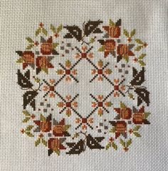 a cross stitch pattern with leaves and flowers in the center on a white cloth background