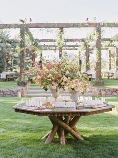 a table with flowers and candles on it in the middle of a grassy area under an arbor