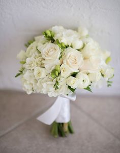 a bridal bouquet with white flowers and greenery on the floor in front of a wall