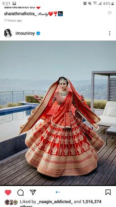 a woman in an orange and red lehenga is standing on a deck near a pool