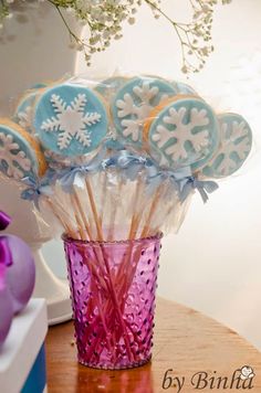 a vase filled with blue and white cookies on top of a wooden table next to purple flowers