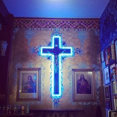 a cross is lit up in the corner of a room with pictures on the wall