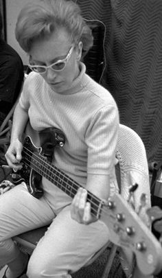 a woman sitting in a chair with a guitar and another person behind her playing the guitar