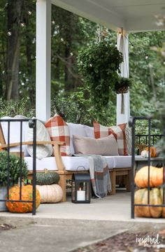 a porch covered in lots of pumpkins and greenery next to a white couch