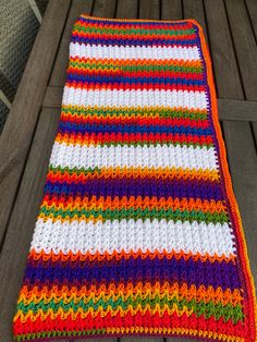 a multicolored crocheted blanket sitting on top of a wooden floor next to a bench