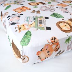 a white sheet with animals on it and a green toy truck in the middle is shown