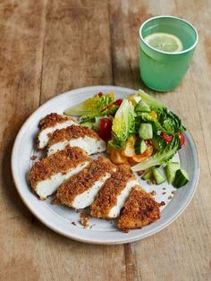 a white plate topped with chicken and salad next to a cup of green tea on top of a wooden table