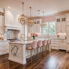 a large kitchen with marble counter tops and white cabinets, gold chandeliers hanging from the ceiling