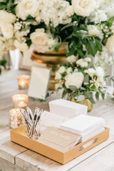 a wooden table topped with lots of white flowers and writing utensils on top of it