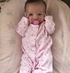 a baby laying on top of a bed with its head in her hands and wearing a pacifier