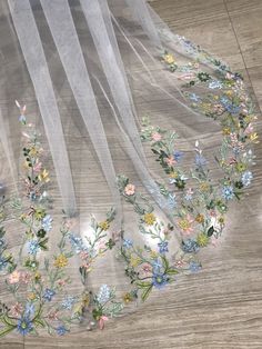 an embroidered veil with flowers and leaves on the bottom is laying on a wooden floor