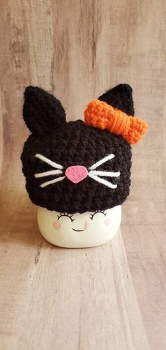 a crocheted black cat hat with an orange bow on it's head