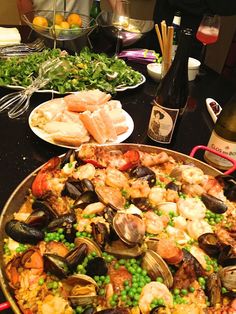 a large pan filled with seafood and vegetables next to wine bottles on a table top