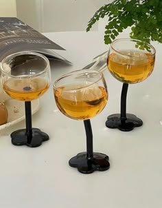 three wine glasses sitting on top of a table next to a potted plant and book