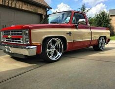 a red and tan truck parked in front of a garage door on a driveway next to a house