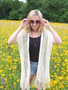 a woman standing in the middle of a field wearing a white crochet cardigan