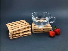 two strawberries sit next to a cup of water and some wooden pallets on a table