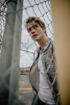 a young man standing next to a fence