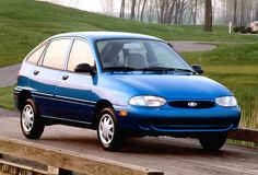 a blue car parked on top of a wooden platform next to a green field and trees