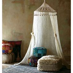 a bed with a white canopy hanging from it's side next to two stools