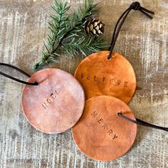 three personalized leather ornaments with pine needles on the top and one is saying believe, merry