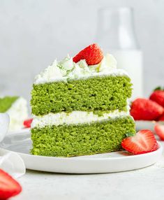 a slice of green cake with white frosting and strawberries on the plate next to it