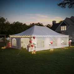 a white tent with lights and balloons on the grass