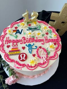 a birthday cake that is decorated with flowers and letters on it, sitting on a table