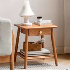 a small wooden table with books and a lamp on it next to a couch in a living room