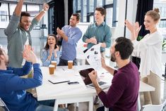 a group of people sitting around a table with their arms in the air and clapping