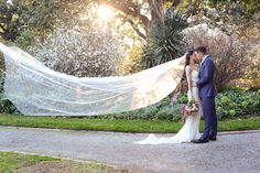 a bride and groom kissing in front of the sun with their wedding veil blowing in the wind