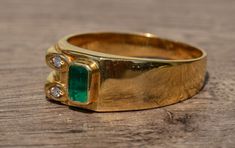 The Greene Street Mid Century Modern Natural Emerald and Diamond Ring. The ring features a bezel set natural Vivid green emerald center measuring 5.2 by 3.2mm. The emerald is a vivid bluish green rich in saturation. To one side of the emerald are two round brilliant cut diamonds in a raised yellow gold tube like section. The ring is crafted in 18 karat yellow gold and is very comfortable to wear. The ring features outstanding stones and is truly a mid century original. The ring is currently a fi Gem Stone Engagement Rings, Vintage Emerald Rings, Ring Worm, Hand Bones, Three Musketeers, Emerald And Diamond Ring, Filigree Engagement Ring, Antique Diamond Rings, Bluish Green