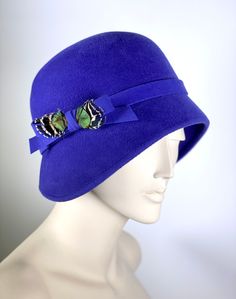 Royal blue winter cloche made of 100% fur felt with a velour finish that is truly soft and luxurious. This hat is trimmed with handmade self fabric band and bow. Complimented with peacock under feathers. A very striking yet simple hat. Custom hat in other colors welcome. Please contact me. This very traditional ladies cloche hat is the perfect dressy casual hat! Small brim with a side pleat, great colors, very stylish! It is hand shaped on a vintage wooden hat block. The hat will fit a 2 1/2 to Cloche Hats, Derby Hats Fascinators, Derby Fascinator, Womens Fedora, Hat Blocks, Rain Hat, Hat Custom, Feather Fascinators, Blue Winter