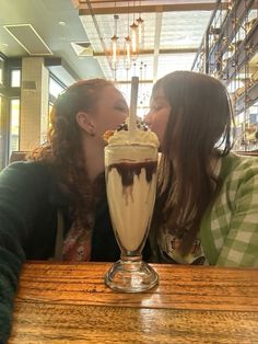 two women kissing each other in front of a milkshake with whipped cream and chocolate