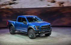 a blue truck is on display at an auto show in front of a large screen