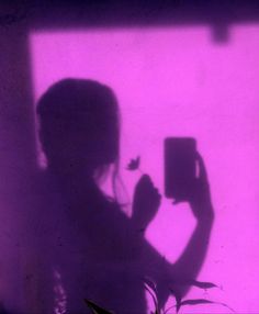 the shadow of a person holding a cell phone in front of a purple light wall