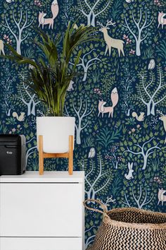 a plant in a pot next to a blue wallpaper with deers and trees