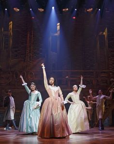 a group of people on stage with their arms in the air and one person wearing a dress