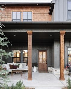 the front porch of a house with wooden pillars and chairs on it's patio