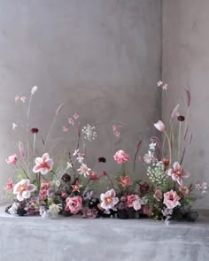 an arrangement of pink and white flowers sitting on top of a gray table next to a wall